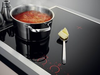 Ein Löffel Butter ruht sicher auf dem Kühlfeld neben einer blubbernden Pfanne Tomatensauce