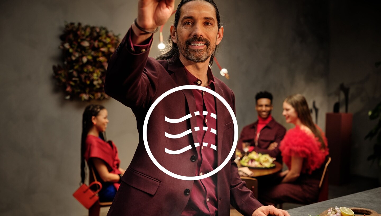 Nahaufnahme eines Mannes auf einer Dinnerparty mit Gästen, die an einem Tisch im Hintergrund sitzen.