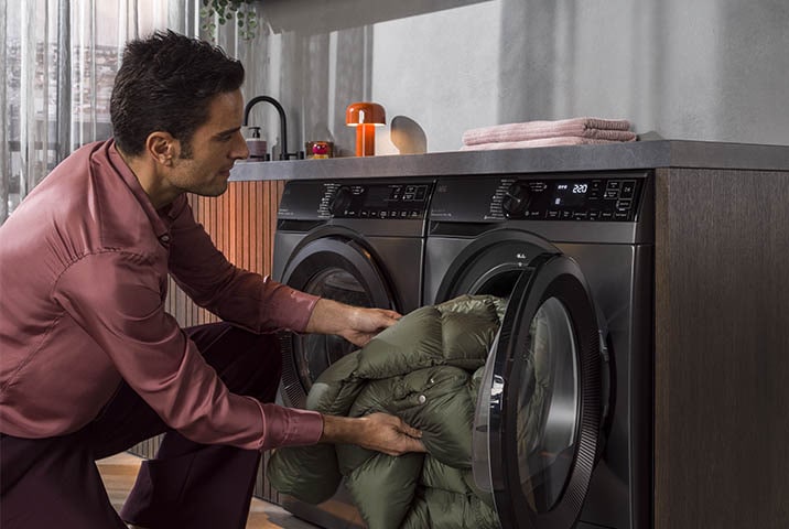 Mann lädt Daunenjacke in AEG Waschmaschine mit großer Trommelkapazität in modernem Hauswirtschaftsraum
