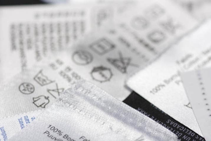 Nahaufnahme von Pflegeetiketten auf Kleidungsstücken mit Wäschepflegesymbolen und Materialangaben