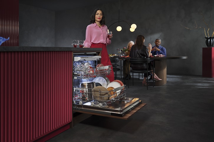 Eine Frau steht in einer modernen Wohnküche vor einem geöffneten Geschirrspüler