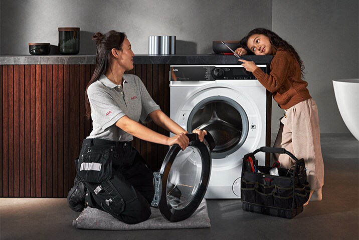 AEG Servicetechnikerin tauscht Türdichtung an AEG Waschmaschine aus, ein junges Mädchen schaut interessiert zu