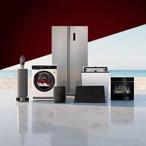 AEG Haushaltsgeräte-Sortiment mit Kühlschrank, Geschirrspüler, Backofen, Induktionskochfeld, Trockner, Heißluftfritteuse und Akku-Staubsauger vor einem hellen Strandhintergrund.